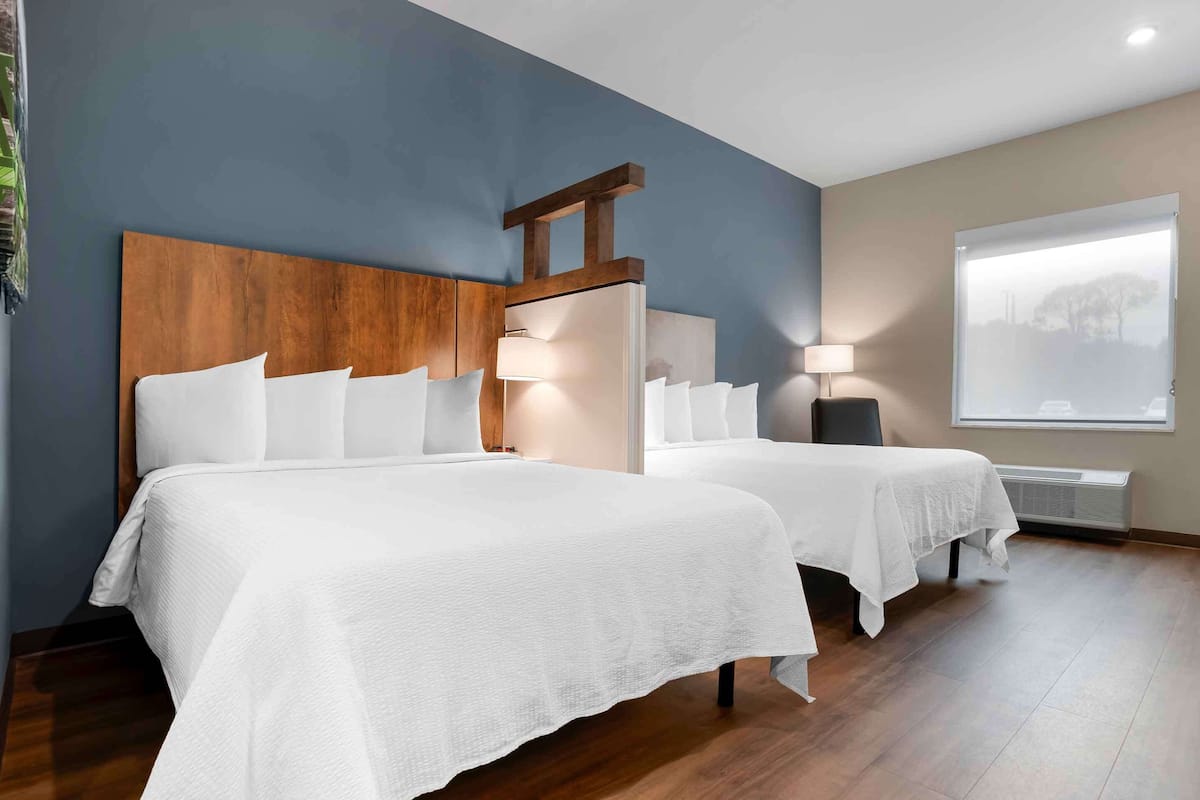 A hotel room with two beds, a wooden headboard, a large window with a view, and a ceiling fan.
