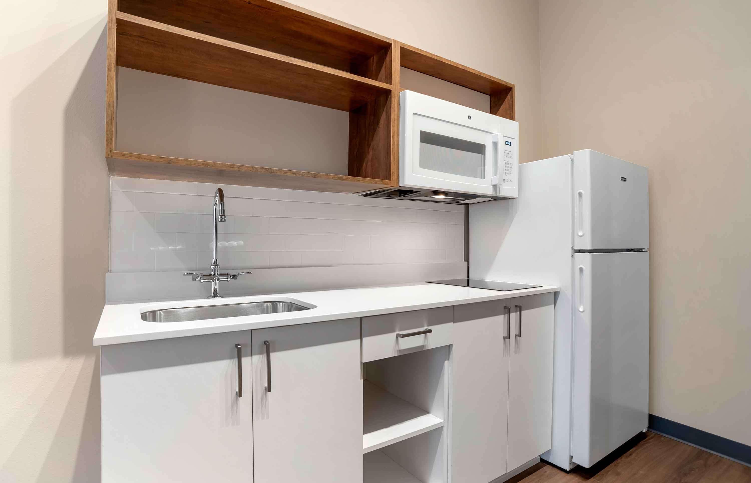 Una cocina con armarios blancos, un lavaplatos de acero inoxidable, un microondas y un refrigerador.