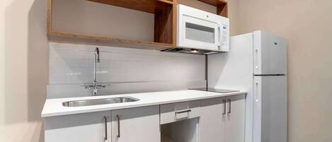 Una cocina con armarios blancos, un lavaplatos de acero inoxidable, un microondas y un refrigerador.
