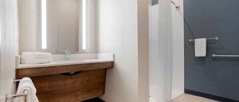 A modern bathroom with a wooden vanity, a large mirror, a glass shower enclosure, and a towel rack.
