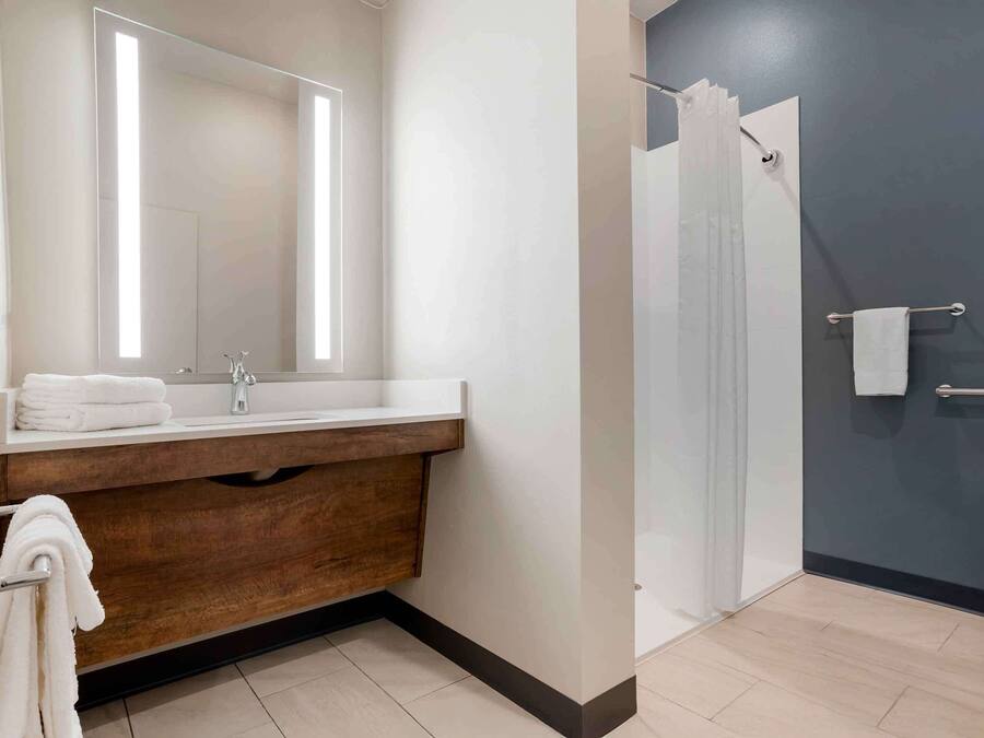 A modern bathroom with a wooden vanity, a large mirror, a glass shower enclosure, and a towel rack.