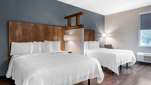 A hotel room with two beds, wooden headboards, a large window, and a wall-mounted air conditioning unit.