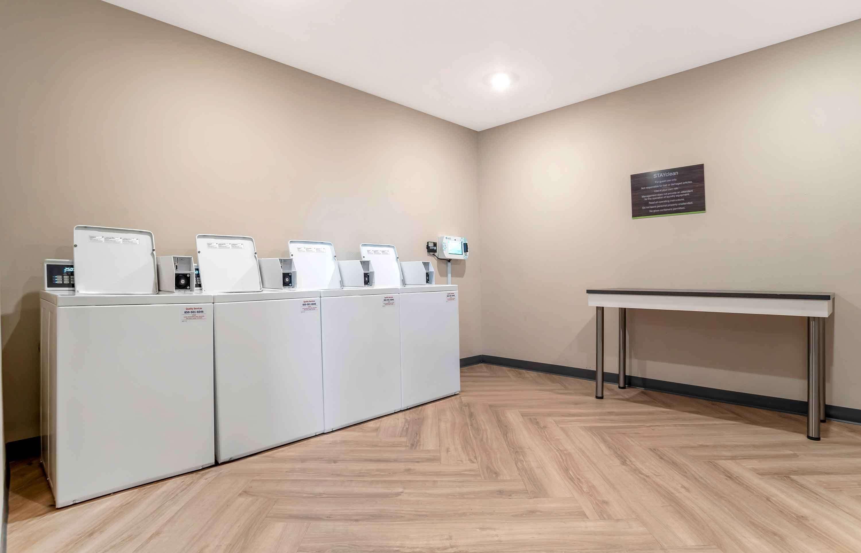 A laundry area with four white appliances, a table, and a wall-mounted sign.