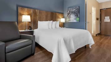 Una habitación de hotel con una cama grande, dos lámparas de noche, un sillón gris y un cabecero de madera.