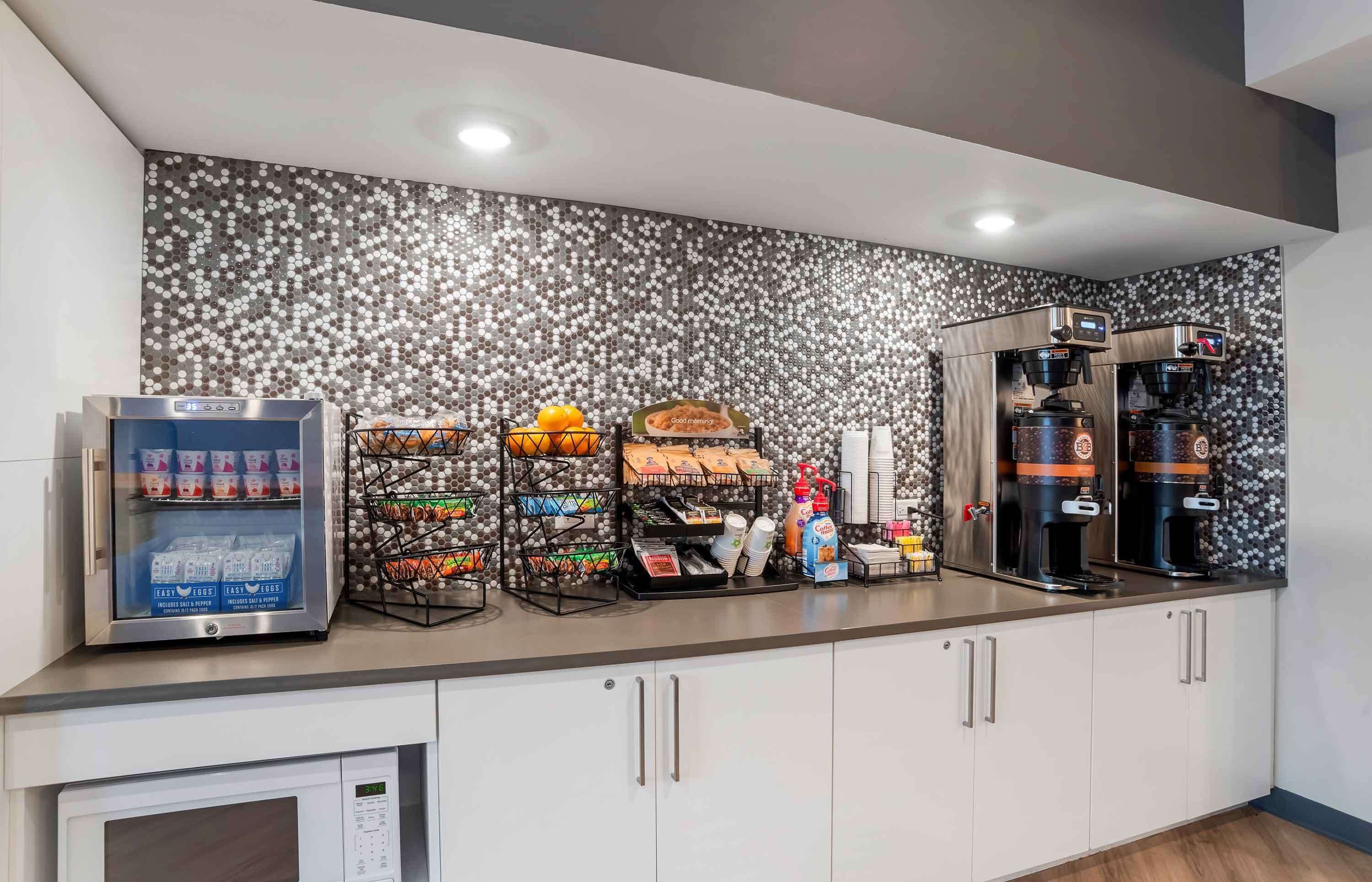 A kitchenette with a coffee machine, a beverage dispenser, and various food items.