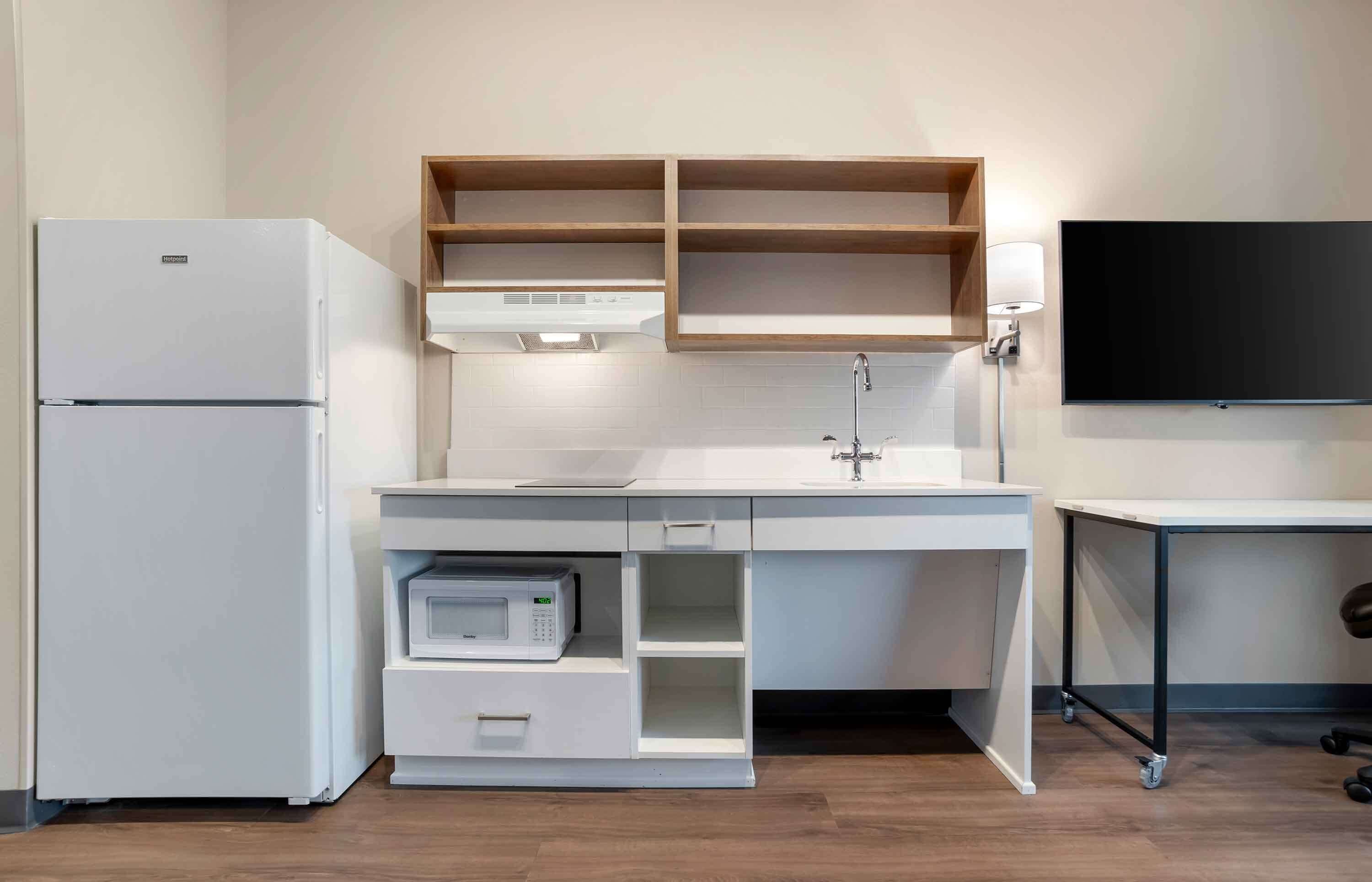 Una kitchenette compacta con refrigerador, microondas y pileta con un alacena superior.