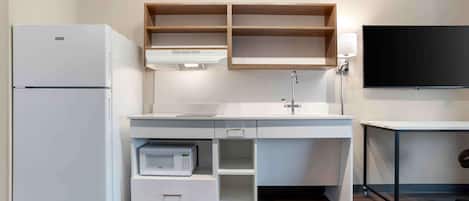A compact kitchenette with a refrigerator, microwave, and a sink with a cabinet above.