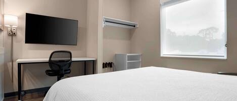 A hotel room with a bed, a desk with a chair, a TV, a window, and a wardrobe.