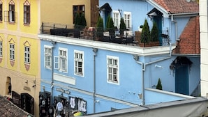 A row of colorful buildings with red-tiled roofs, a visible shop on the ground floor, and a balcony with railings. - Blue House Citadel Sighisoara (Sighisoara)