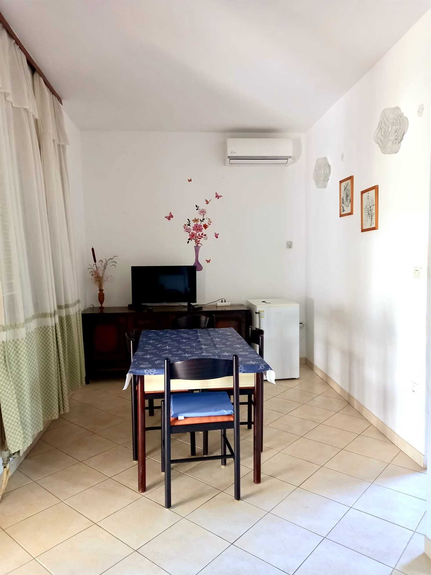 A dining area with a table, chairs, a TV, and a refrigerator.