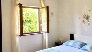 A bedroom with a bed, a nightstand, a window with curtains, and a wall with a floral decoration. - Apartment Tea 2 close to the beach and city center (Umag)