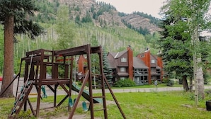 A playground with swings and a slide, a building with a red roof, and a mountainous backdrop. - Stylish 2 BR & 2 bath + Loft Durango Condo near Purgatory (Durango)