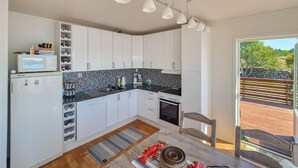 A compact kitchen with white cabinets, a black countertop, and a built-in oven. There is a small dining area with a wooden table and a chair. - Cozy home in Sveio with WiFi (Sveio)