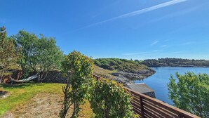 A coastal view with a wooden deck overlooking a calm body of water, surrounded by greenery and rocky terrain. - Cozy home in Sveio with WiFi (Sveio)