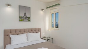 Ein Hotelzimmer mit einem großen Bett, einem gerahmten Bild des Eiffelturms, einem kleinen Tisch und einem Fenster mit Blick.