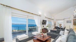 Ein modernes Wohnzimmer mit einer Couch, einem Couchtisch und einem Fernseher. Es besitzt einen Balkon mit Meerblick.