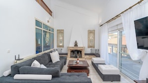 Ein modernes Wohnzimmer mit Kamin, grauen Sofas, einem Couchtisch und einem großen Fenster mit Vorhängen.