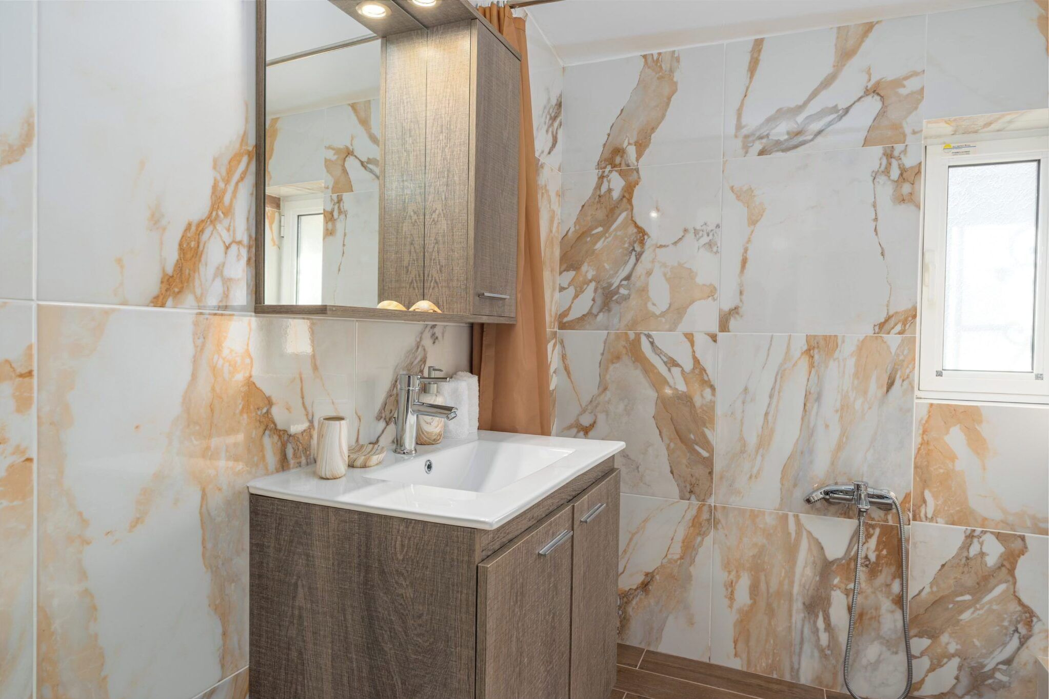A bathroom with a marble backsplash, a wooden vanity, a sink, a mirror, and a shower.