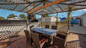 An outdoor patio with a glass-top table and wicker chairs, surrounded by a wooden pergola and a lattice fence. - BOOK NOW!!! Your vacation awaits your home for Disneyland and OC destinations. (Anaheim)