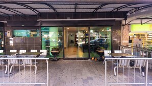 Een restaurant met terras, een overdekte ingang en een zichtbaar interieur door de glazen deuren.