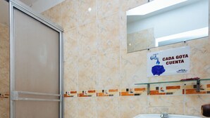 Een badkamer met toilet, wastafel en douche. Een bord boven de wastafel geeft de tekst weer: CADA GOTA CUENTA.