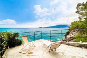 Un patio de piedra con dos sillones de descanso con vistas al mar turquesa y a la costa rocosa.