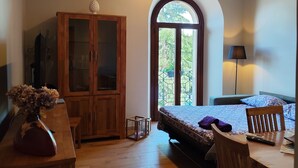 Quarto com teto de madeira, cama com colcha estampada, armário de madeira, pequena mesa com um vaso e uma luminária.