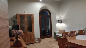 Uma sala de jantar com uma mesa e cadeiras de madeira, um armário com portas de vidro, um abajur e uma vista através de uma porta em arco.