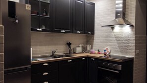 Uma cozinha moderna com armários escuros, uma geladeira de aço inoxidável, forno embutido e teto com padrão de tijolos.