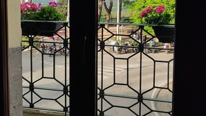 Vista de uma varanda com guarda-corrimão de metal, piso de azulejos e cerca verde.