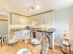 Una cocina moderna con armarios blancos, electrodomésticos de acero inoxidable y una zona de comedor preparada para seis personas, con una mesa redonda y sillas.