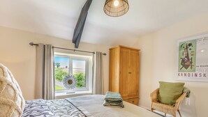 Une chambre à coucher avec un grand lit, une armoire en bois, un fauteuil en osier et une vue sur l’extérieur par une fenêtre.