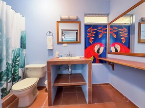A bathroom with a toilet, sink, and mirror. There is a towel rack and a window with curtains.