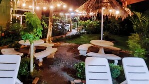 Un área de estar al aire libre con sillones blancos y una estructura de techo de paja.