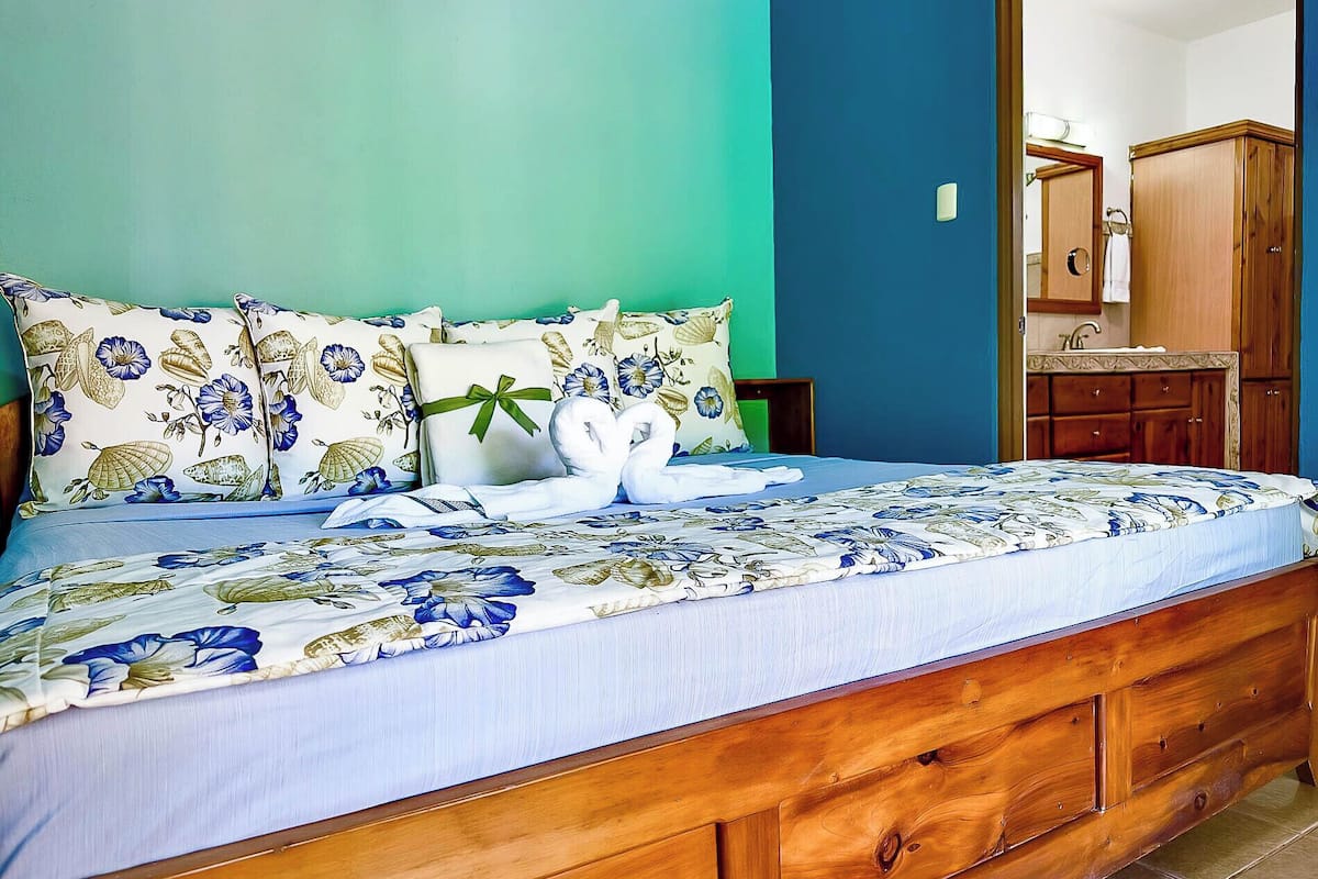 A bedroom with a floral bedspread, two white towels arranged as swans, and a wooden headboard.