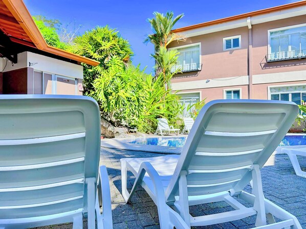 Two white lounge chairs facing a swimming pool with a building in the background.