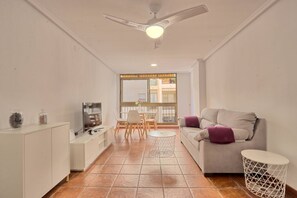A modern living room with a sofa, a coffee table, a TV, and a dining area with chairs and a table. - 063 - Club Náutico 006 - comfortHOLIDAYS (Santa Pola)