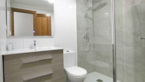 A modern bathroom with a glass shower enclosure, a white toilet, and a vanity with a mirror and sink. - 063 - Club Náutico 006 - comfortHOLIDAYS (Santa Pola)