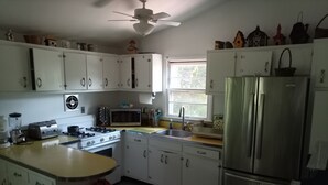 Une cuisine avec des meubles blancs, une cuisinière, un four à micro-ondes, un évier et un réfrigérateur.