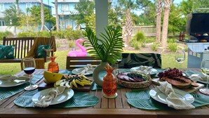 Een gedekte tafel voor een maaltijd met tropisch fruit, een flamingo drijvend object en een barbecue op de achtergrond.