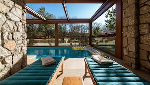 Un área junto a la piscina con muros de piedra, una terraza de madera y sillones de descanso.