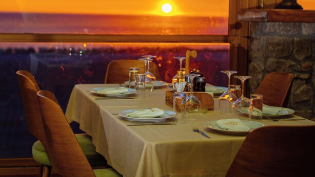 Mesa de comedor para dos con vista a un atardecer a través de un ventanal grande.