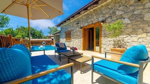 Un edificio de piedra con piscina, muebles azules y una sombrilla grande.