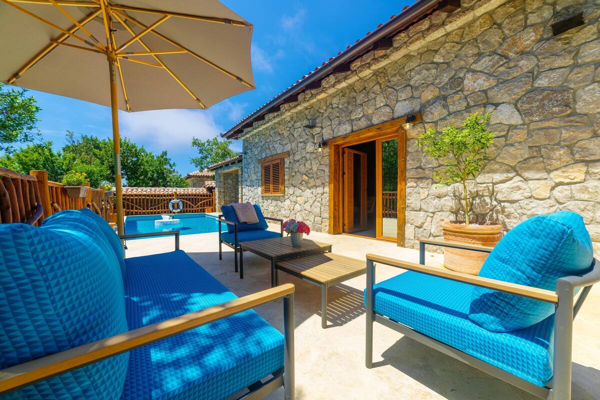 A stone building with a pool, blue furniture, and a large umbrella.