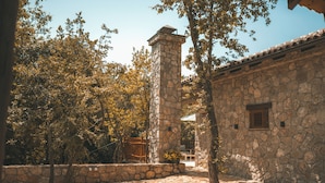 Un edificio de piedra con una torre central, rodeado de árboles y un muro de piedra.