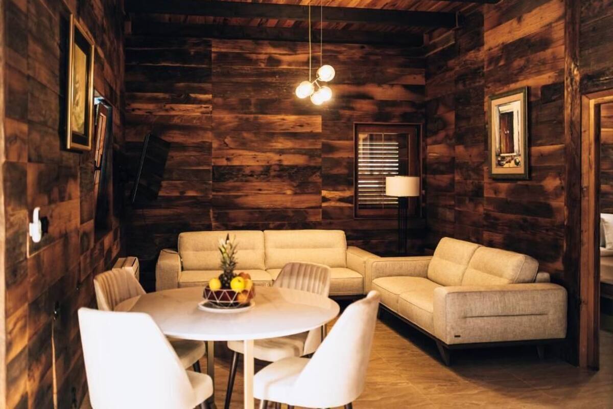 A cozy room with a wooden interior, a round table with chairs, a sofa, and a hanging light fixture.