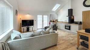 Ein modernes Wohnzimmer mit einem grauen Sofa, einem Flachbildfernseher und einem Essbereich mit einem kleinen Tisch und Stühlen.