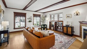 A living room with a brown leather sofa, a round coffee table, and a patterned rug. There is a bookshelf with decorative items and a fireplace.