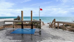Eine Holzterrasse mit einer blauen Matte, einer roten Flagge und Blick auf das Meer.