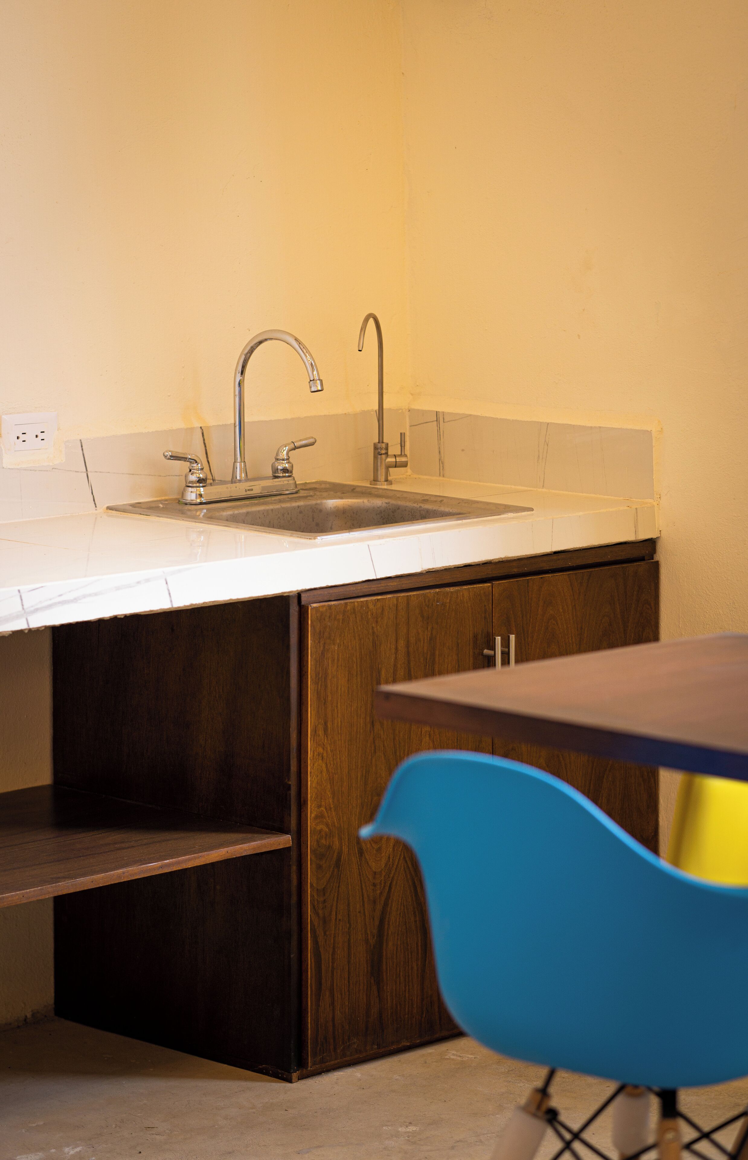 A kitchen with a double sink, wooden cabinets, and a blue chair.
